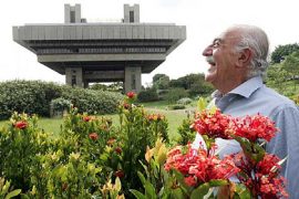 Gian Carlo Gasperini à frente de prédio que projetou, junto a um jardim florido PCV